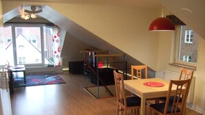 Een eetgedeelte met een houten tafel en stoelen, een rode hanglamp en uitzicht op een gebouw door een raam.