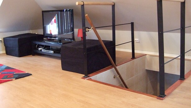 Een kamer met een schuine plafond, een televisie, een zwart poef en een houten constructie.