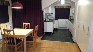 Een compacte keuken met een eethoek, met een tafel en stoelen, een rode hanglamp en een donker gordijn.