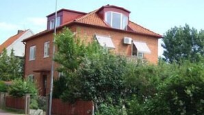 Een twee verdiepingen tellend bakstenen huis met een rood dak, een klein balkon en een rode omheining.