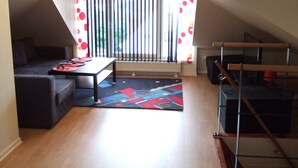 Een gezellig zolderkamer met een donkere bank, een klein tafeltje en een kleurrijk vloerkleed.