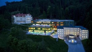 A multi-story hotel with a swimming pool, surrounded by forested hills.