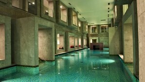 A long, narrow indoor swimming pool with a tiled floor and walls, and multiple seating areas along the sides.