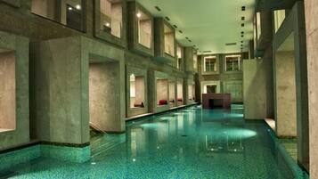 A long, narrow indoor swimming pool with a tiled floor and walls, and multiple seating areas along the sides.