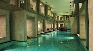 A long, narrow indoor swimming pool with a tiled floor and walls, and multiple seating areas along the sides. - Hotel Zdraviliski Dvor (Lasko)