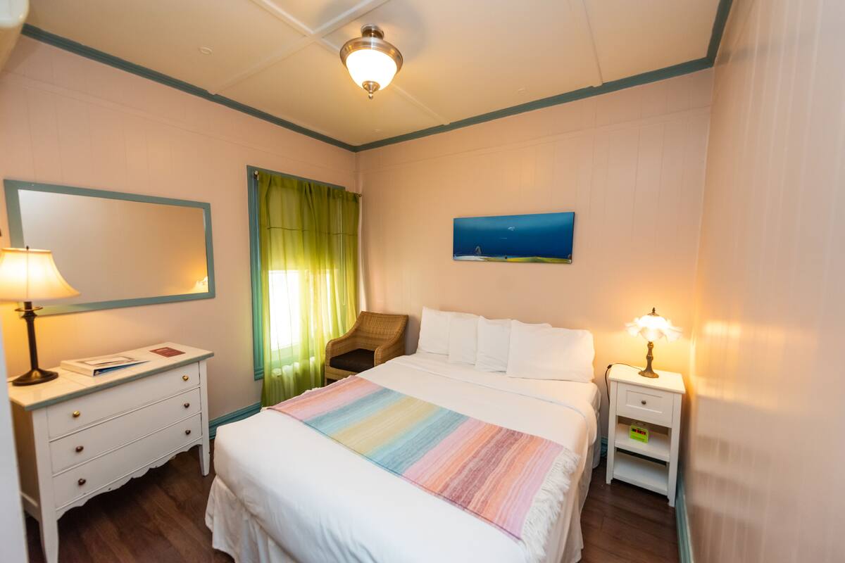 A hotel room with a bed, a nightstand, a chair, a mirror, and a painting on the wall.