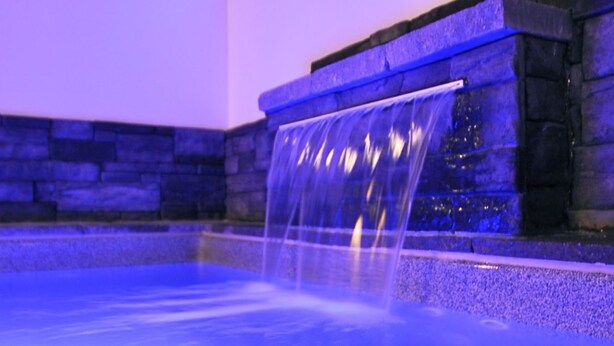 Una piscina con una cascada, paredes de piedra e iluminación azul en el techo.