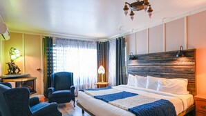 Una habitación de hotel con una cama grande, dos sillones, un cabecero de madera, una mesita de noche y una lámpara.