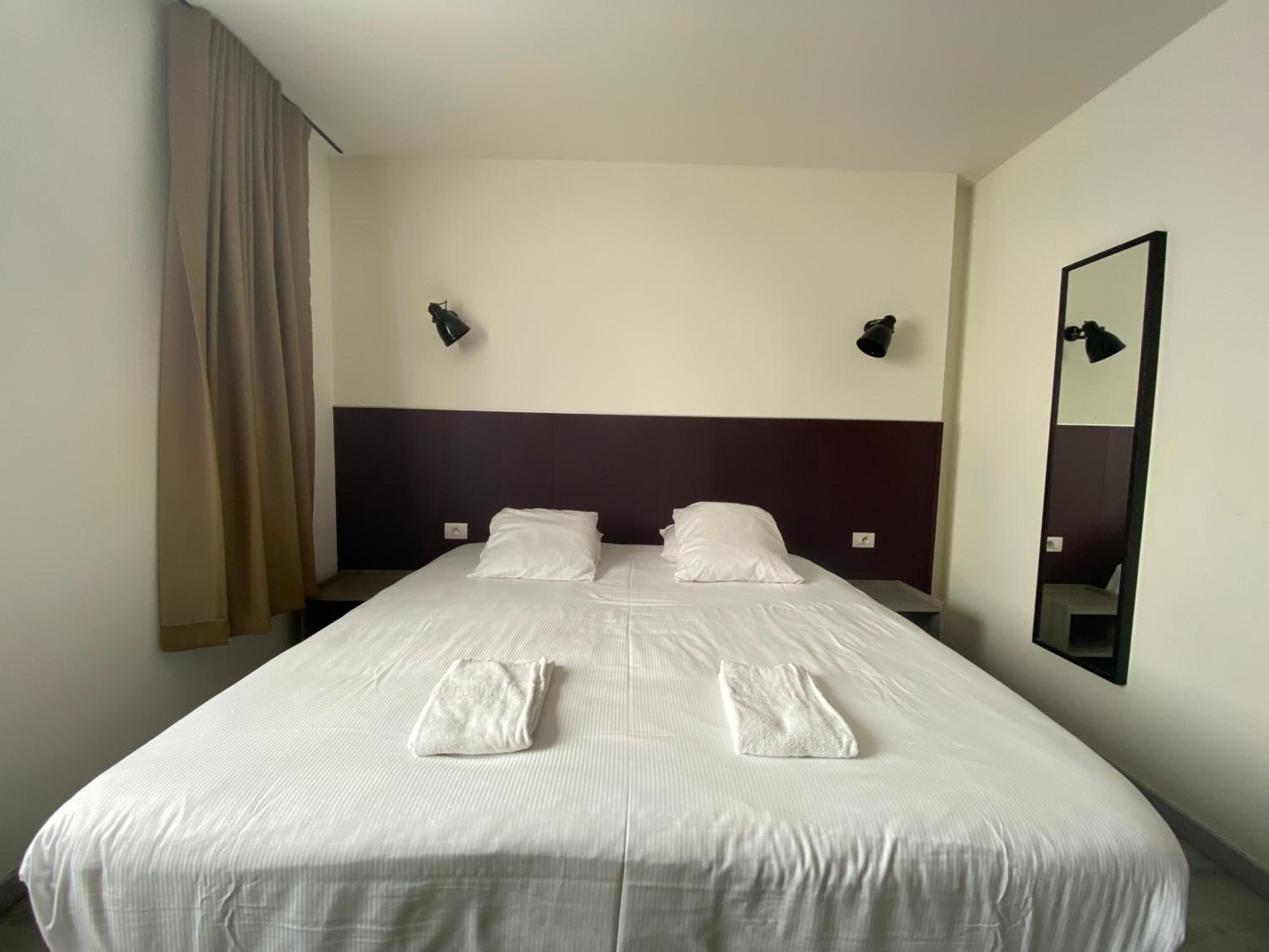 Una habitación de hotel con una cama grande, dos lámparas de noche, un espejo y una ventana con cortinas.