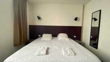 Una habitación de hotel con una cama grande, dos lámparas de noche, un espejo y una ventana con cortinas.