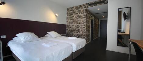 Habitación de hotel moderna con dos camas, una pared decorada con piedra, un espejo y un escritorio.