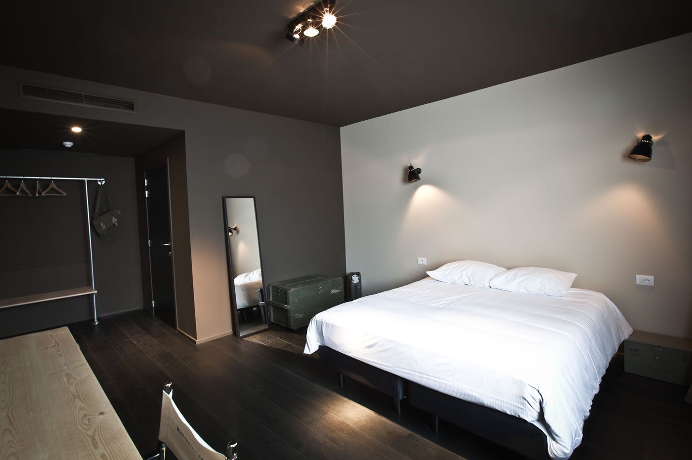 Quarto moderno com uma cama grande, cômoda, espelho e guarda-roupa.