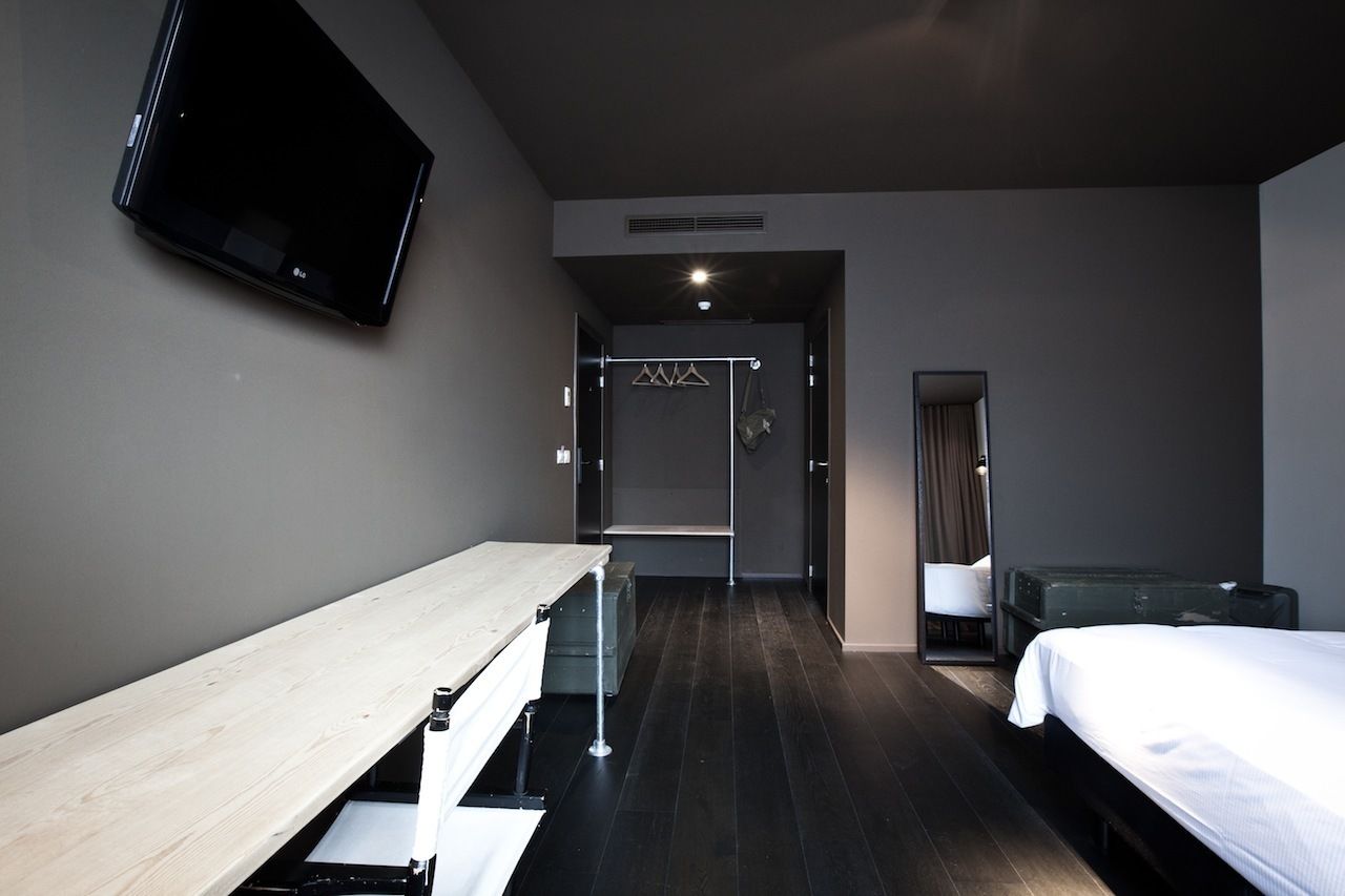 A modern hotel room with a bed, a desk, a TV mounted on the wall, and a wardrobe.