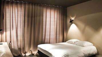 A hotel room with a bed, a desk with a lamp, and two wall-mounted lights.