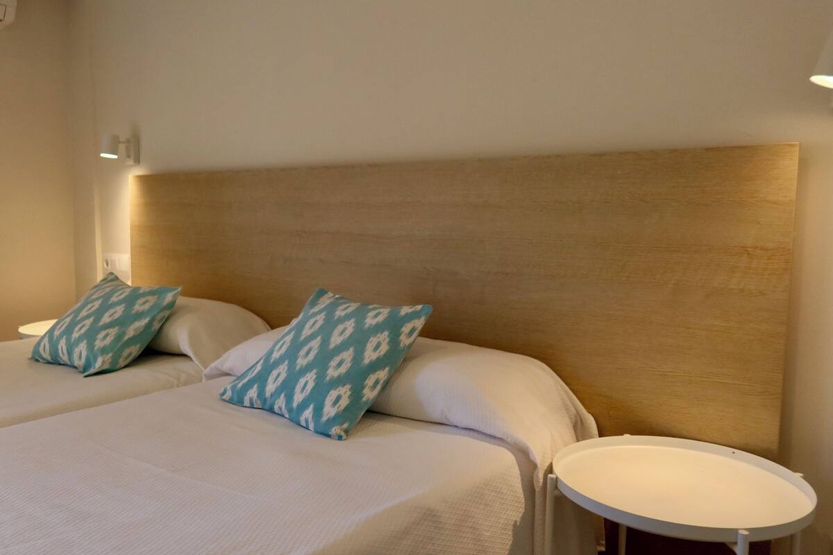 A hotel room with two beds, a round table, and a wall-mounted light fixture.