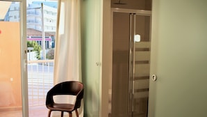 Ein Zimmer mit einer Schiebetür zum Balkon, einer Duschkabine und einem Stuhl.
