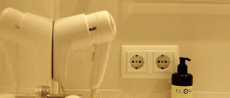 A bathroom with a white sink, a mirror, a hairdryer, and a bottle of hand soap.