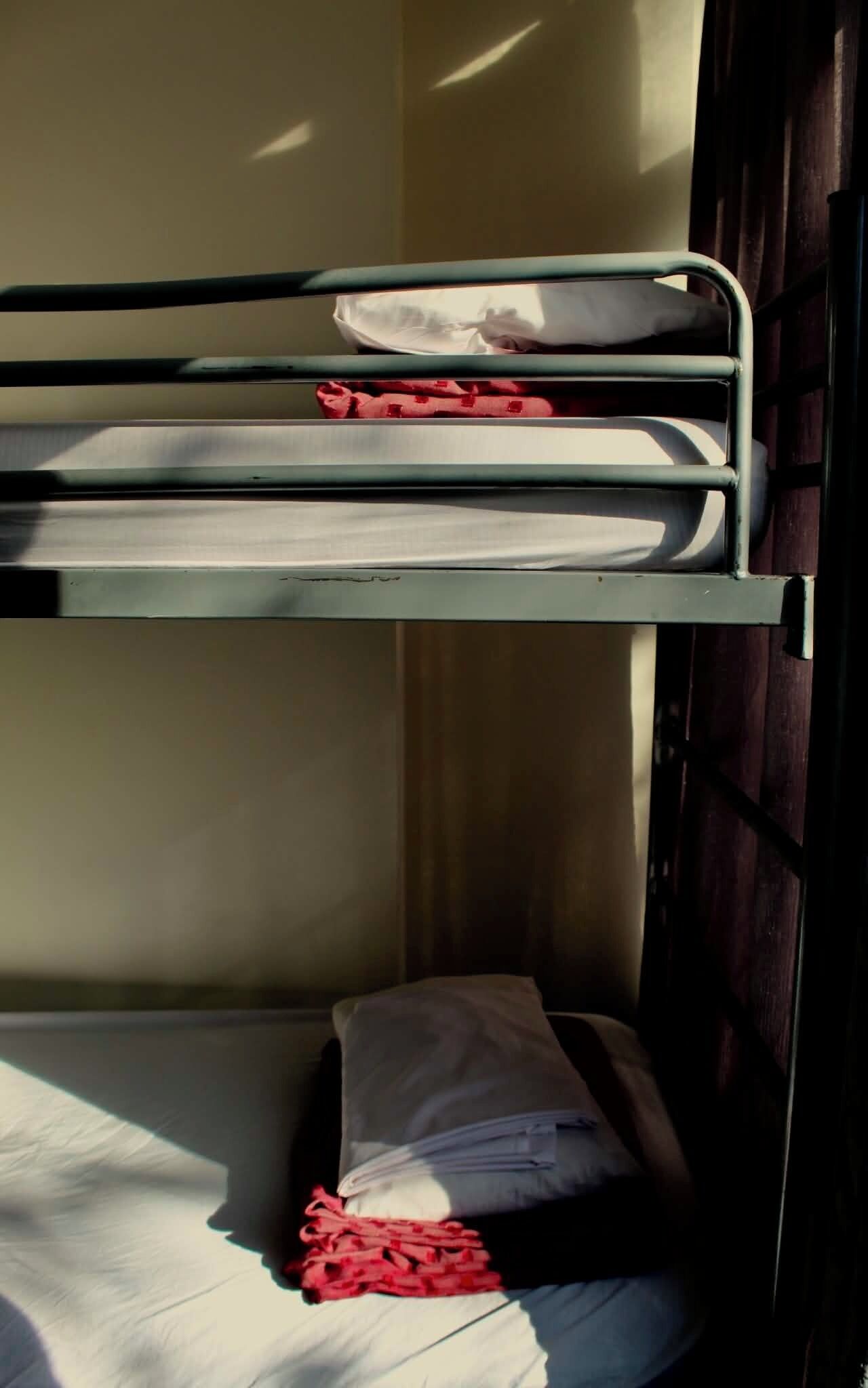 Una cama nido con colchón y almohadas, una puerta de madera y un ventanal.