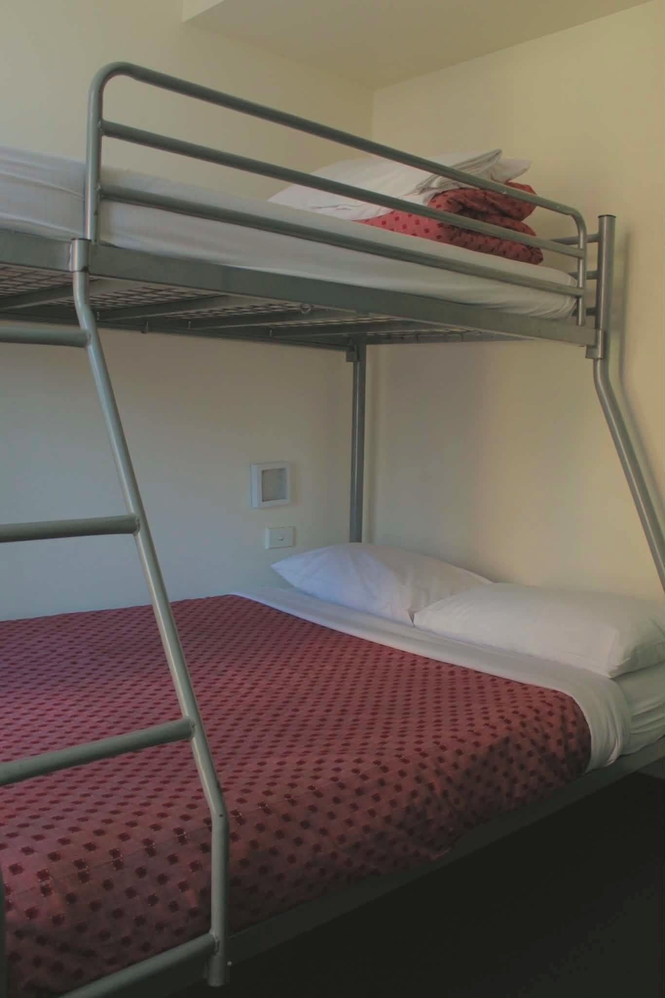 Una cama litera con una escalera, una almohada blanca y una colcha roja con estampado.