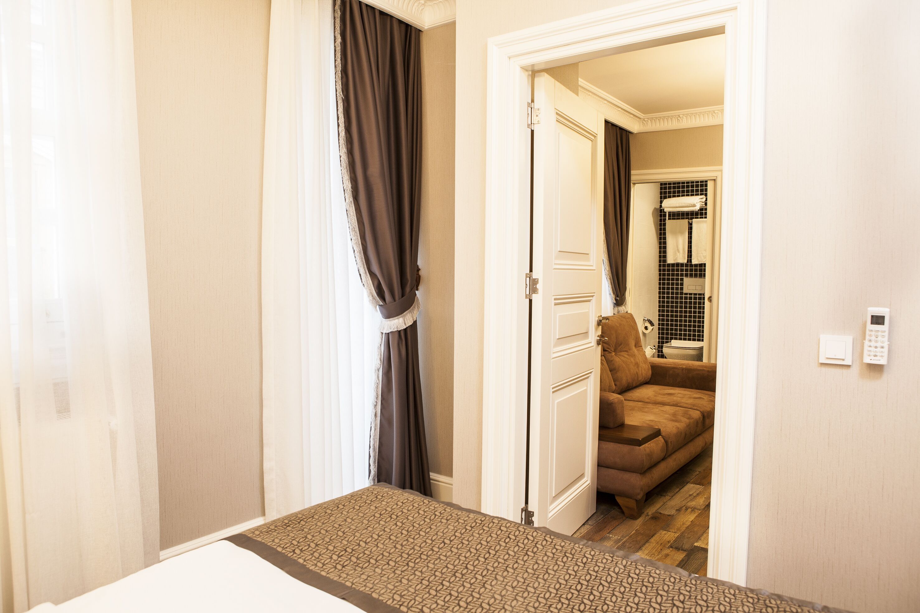 A hotel room with a bed, a door leading to a bathroom, and a brown sofa in the adjacent room.