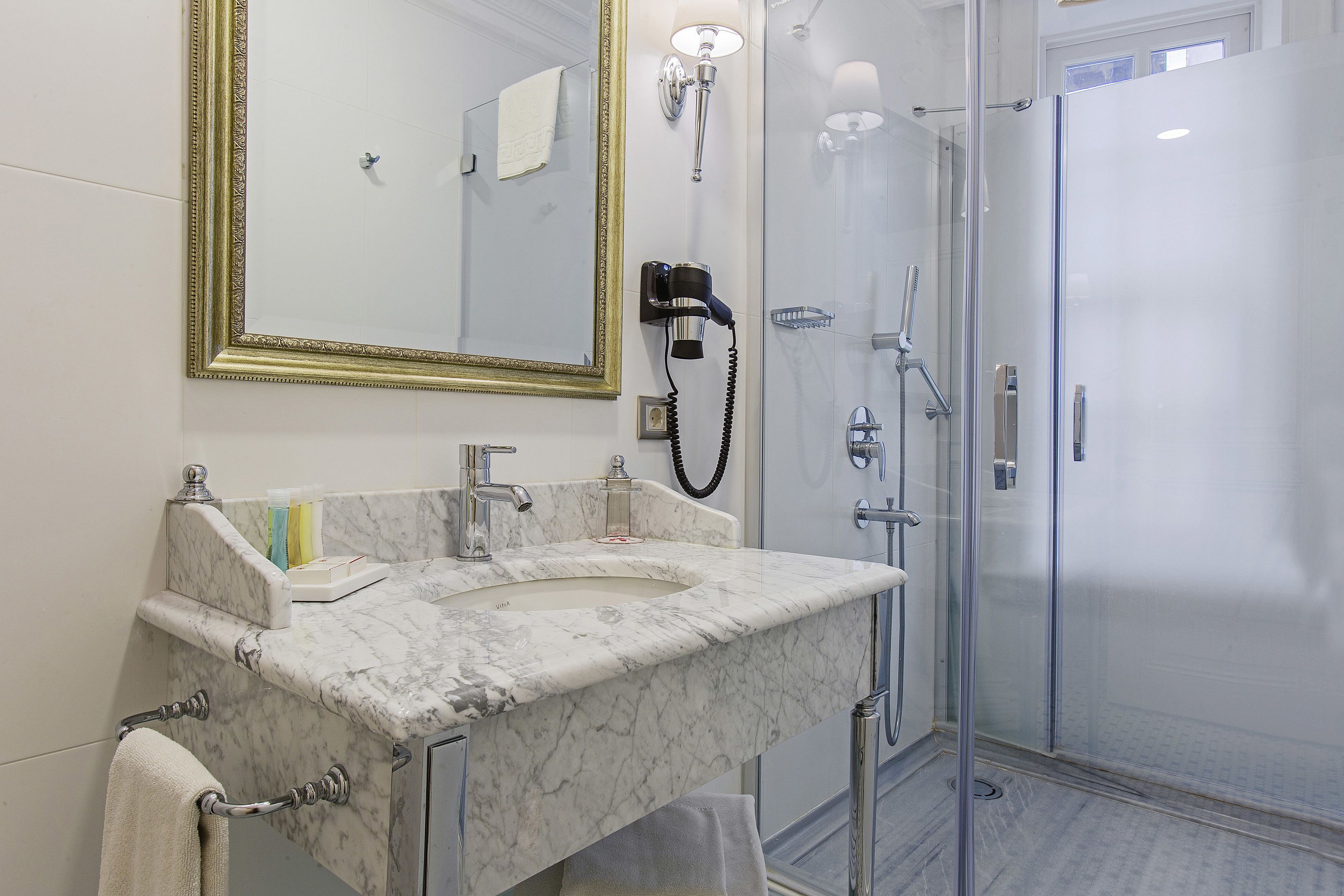 A bathroom with a marble sink, a large mirror, a hairdryer, and a glass-enclosed shower.