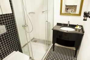 A bathroom with a glass-enclosed shower, a black and white tiled floor, a sink with a black vanity, and a mirror with a gold frame.