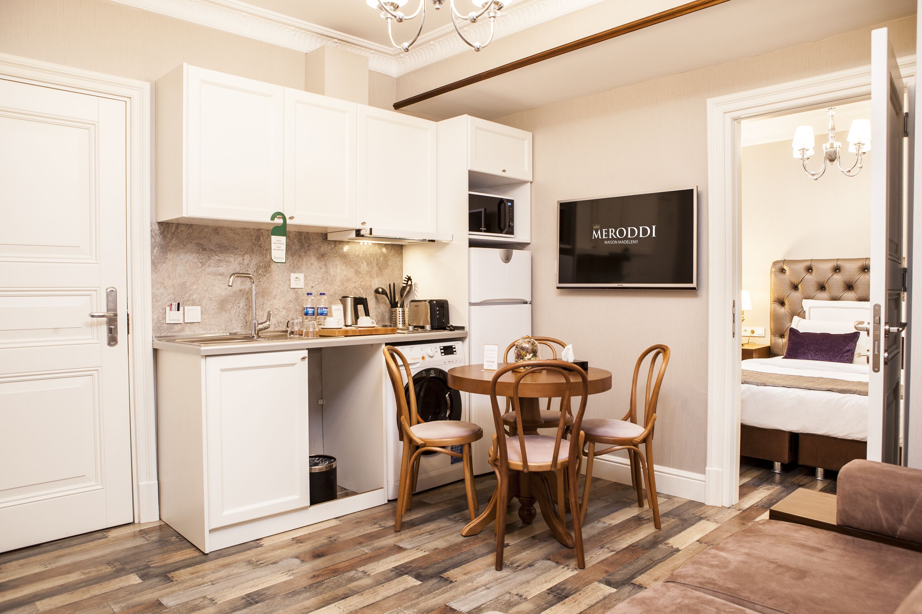 A compact kitchen with white cabinets, a dining table with four chairs, and a modern chandelier.