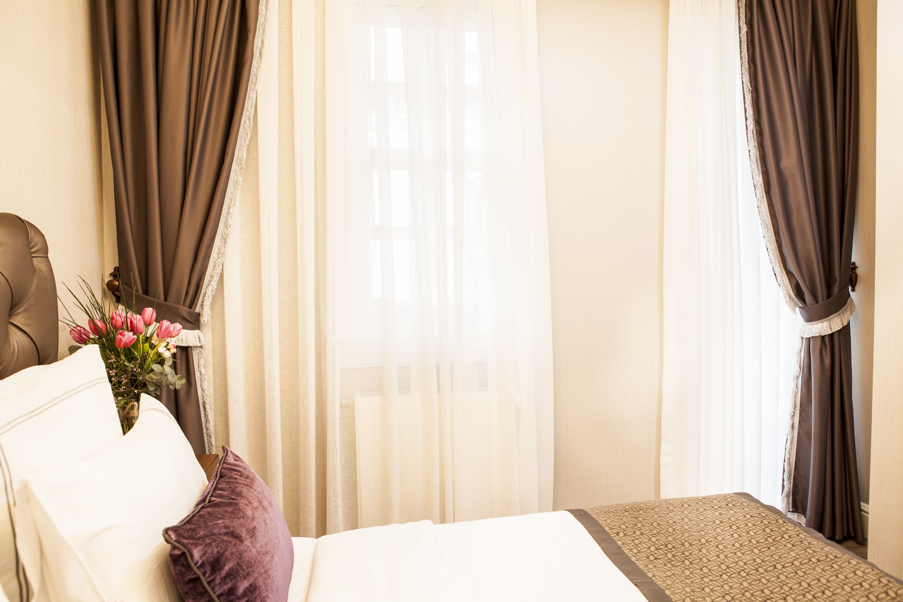 A hotel room with a bed, a chair, a small table, and a vase of flowers.