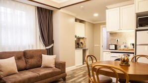 A living room with a brown sofa, wooden dining table, and chairs. There is a kitchen area with white cabinets and appliances. - Meroddi Pera Flats (Istanbul)