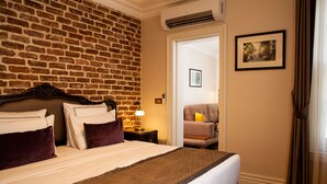 A hotel room with a brick wall, a bed with white and brown bedding, a nightstand with a lamp, and a door leading to another room. - Meroddi Pera Flats (Istanbul)