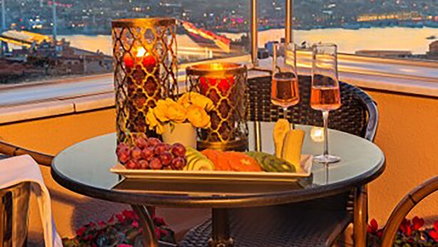 A table with a fruit platter, two glasses of wine, and a decorative candle on a balcony overlooking a cityscape at sunset. - Meroddi Pera Flats (Istanbul)