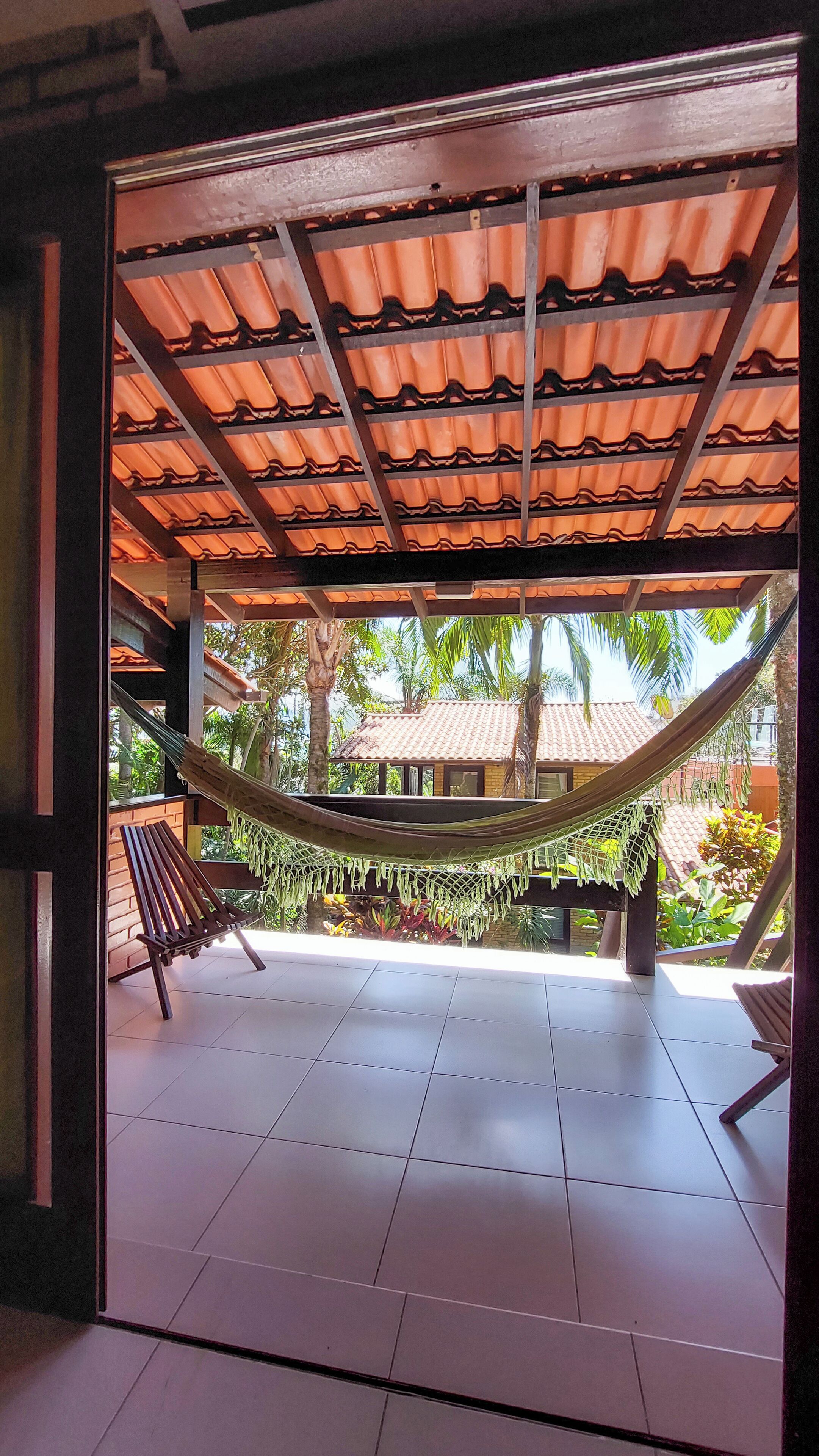A covered outdoor area with a hammock, wooden benches, and a tiled floor.
