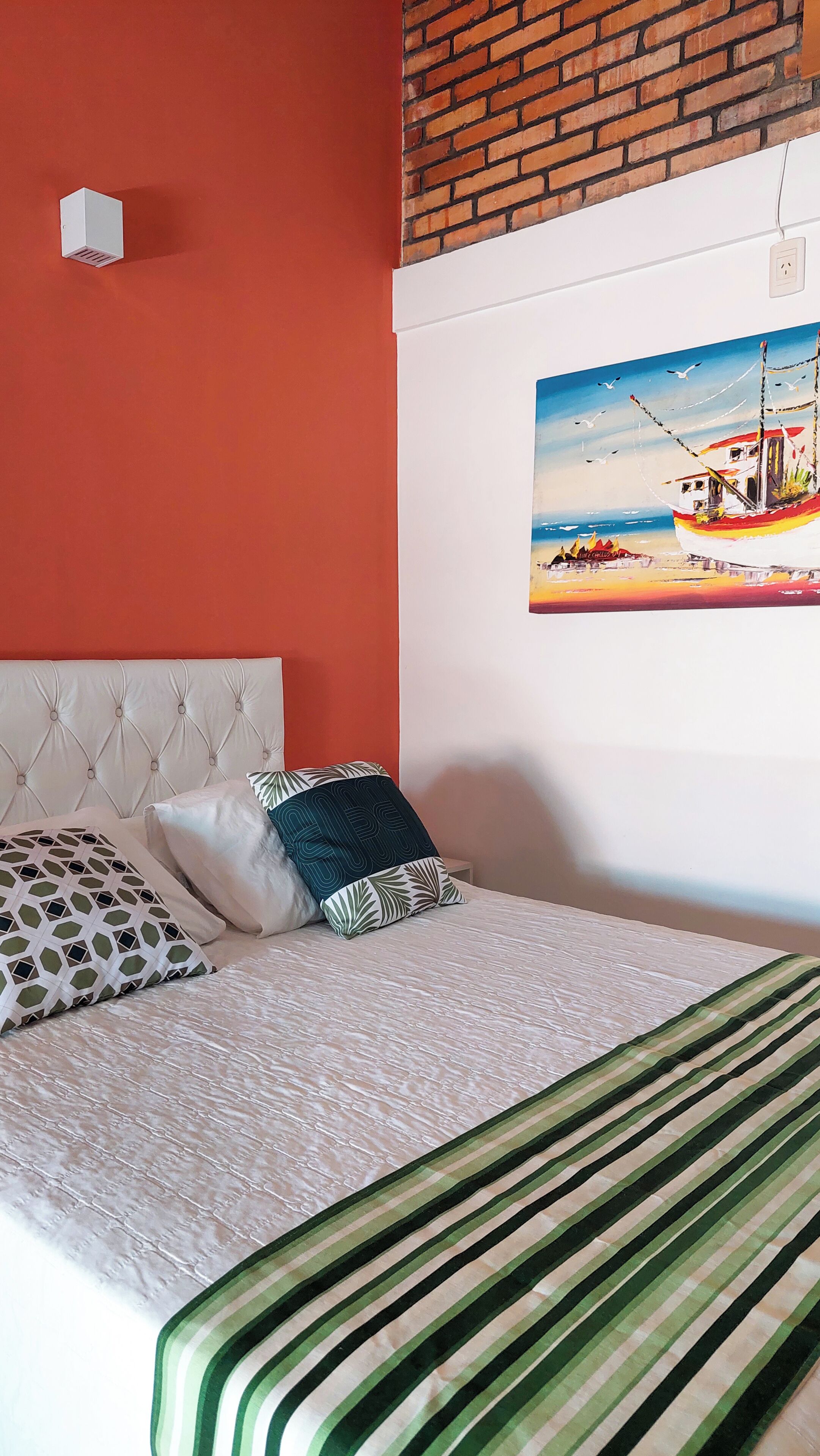 Una cama con un edredón a rayas, un cabecero capitonado y almohadas estampadas.