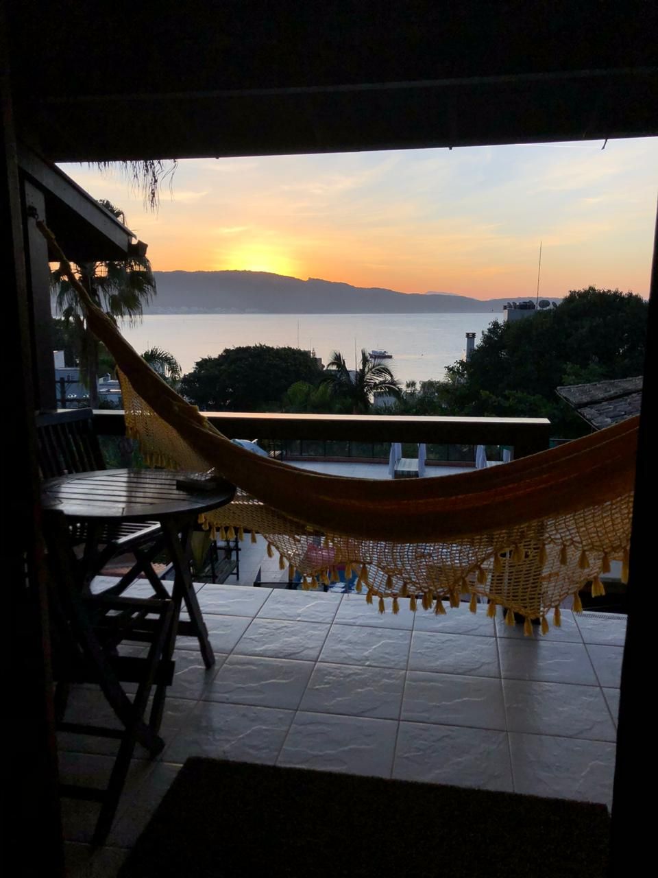 A hammock on a balcony overlooking a body of water during sunset.