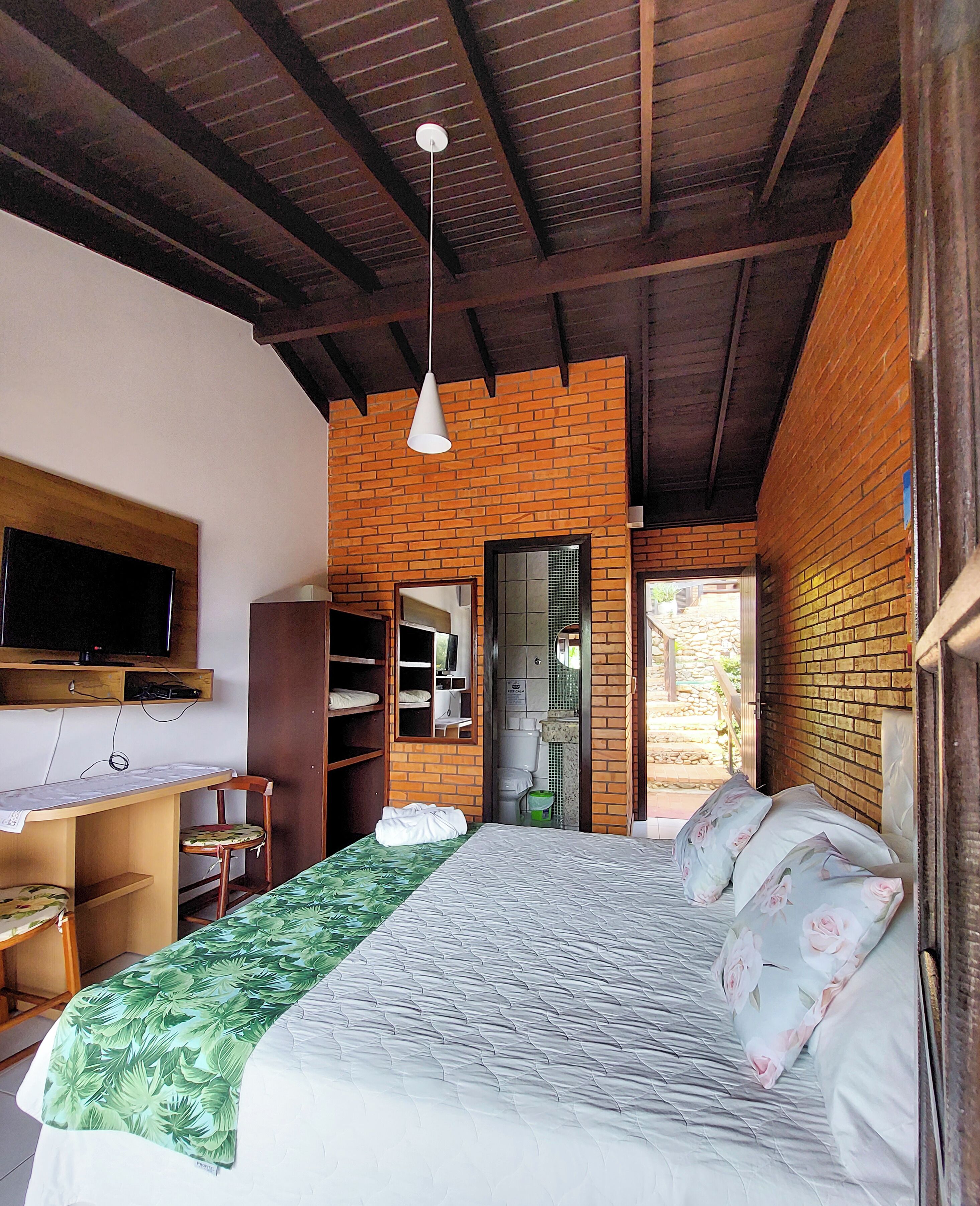 A bedroom with a bed, a desk, a chair, a television, and a brick wall.
