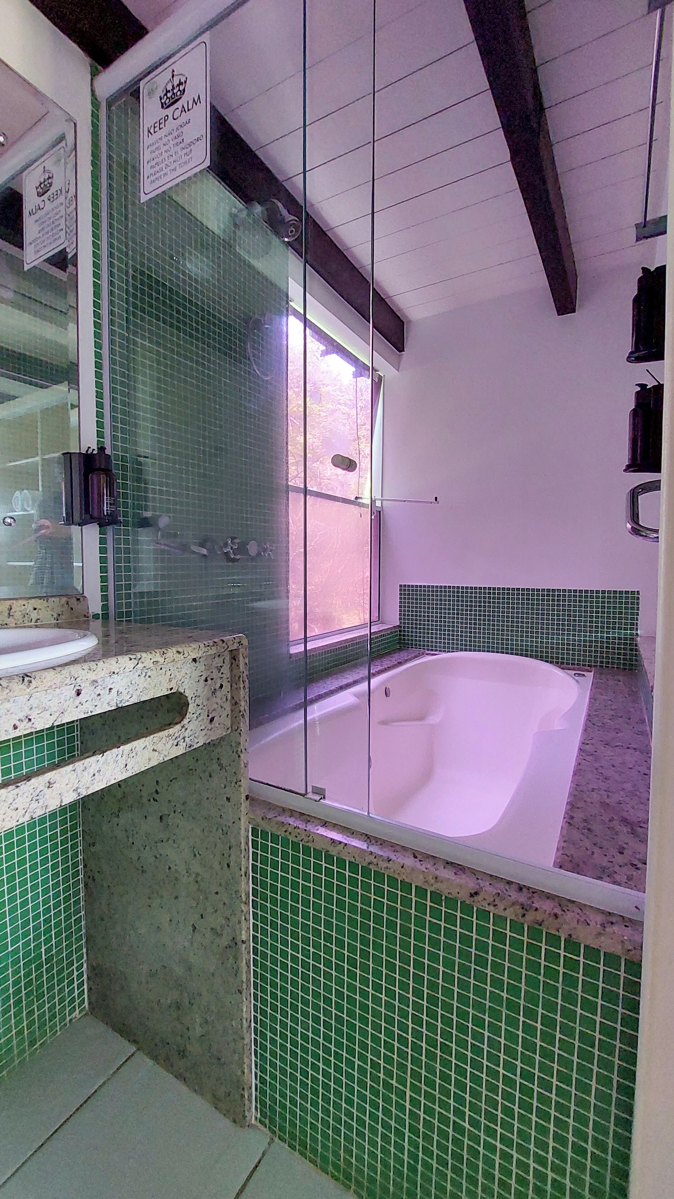 A bathroom with a bathtub, green tiled walls, a sink, and a mirror.