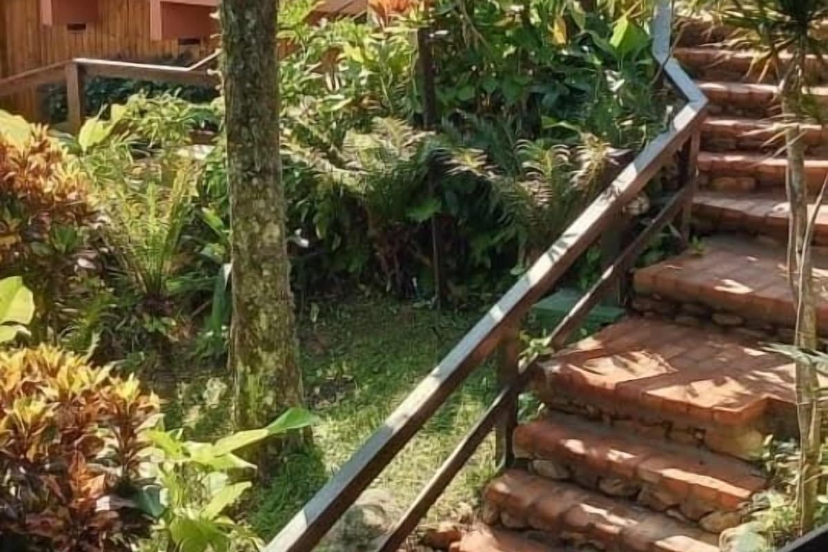 A staircase with a metal railing leading to a covered area with plants and a building in the background.