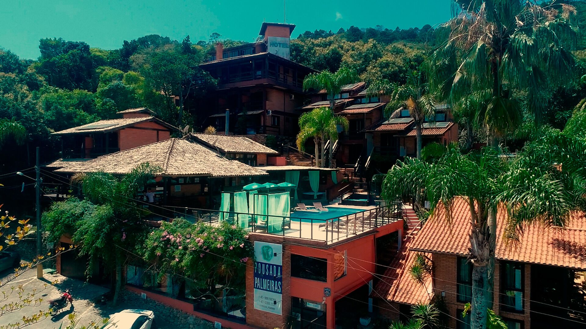 Un hotel con varias construcciones, piscina y abundante vegetación.