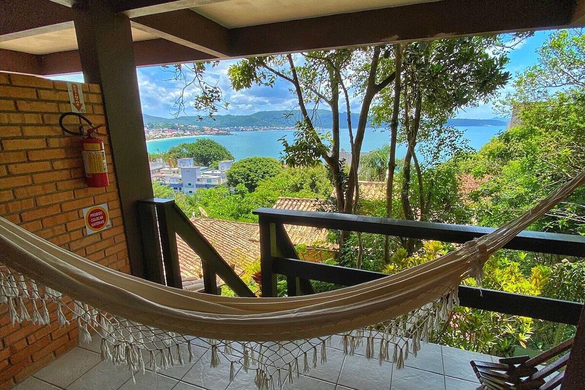 A balcony with a hammock, a fire extinguisher, and a view of the sea and greenery.