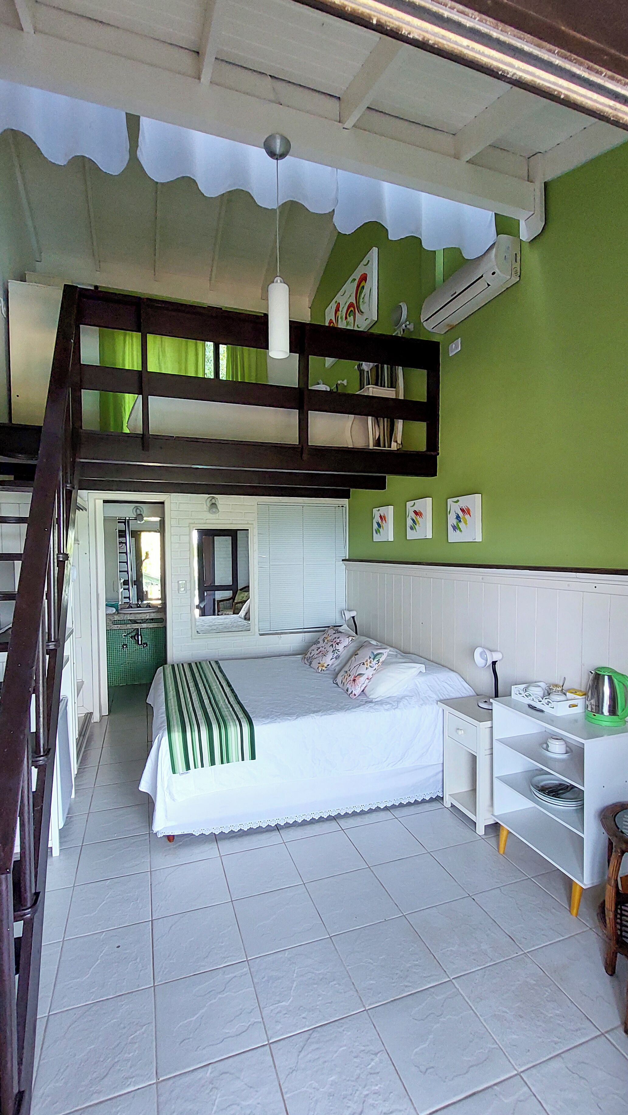 Una habitación con una cama doble, un escritorio, una silla, una estantería con utensilios de cocina y una ventana con cortinas.