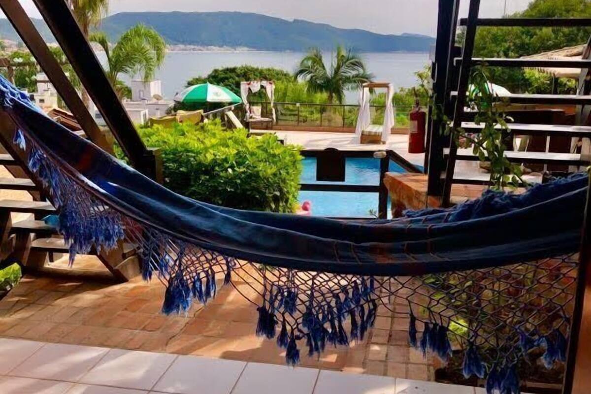 A hammock on a tiled balcony overlooking a swimming pool and a mountainous landscape.