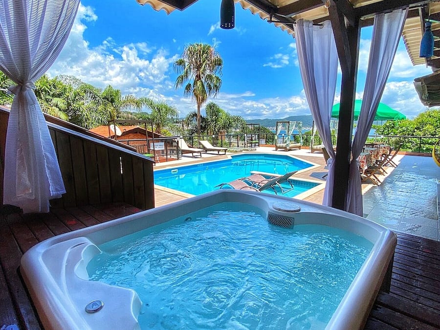 Uma banheira de hidromassagem sob uma área coberta, com piscina e espreguiçadeiras.