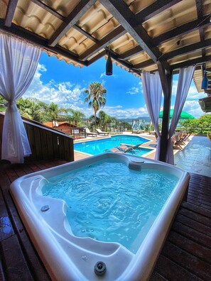A hot tub under a covered area with a pool and lounge chairs. - Pousada Palmeiras (Bombinhas)
