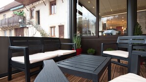 A balcony with a wooden table and two black chairs with white cushions. - La Table de Gustave (Ornans)