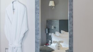 A hotel room with a bed, a nightstand, a lamp, and a robe hanging on the wall. - La Table de Gustave (Ornans)