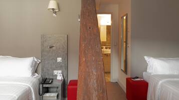 Habitación de hotel con dos camas, un reposapiés rojo, un pilar de madera, un escritorio con teléfono y un espejo en la pared.