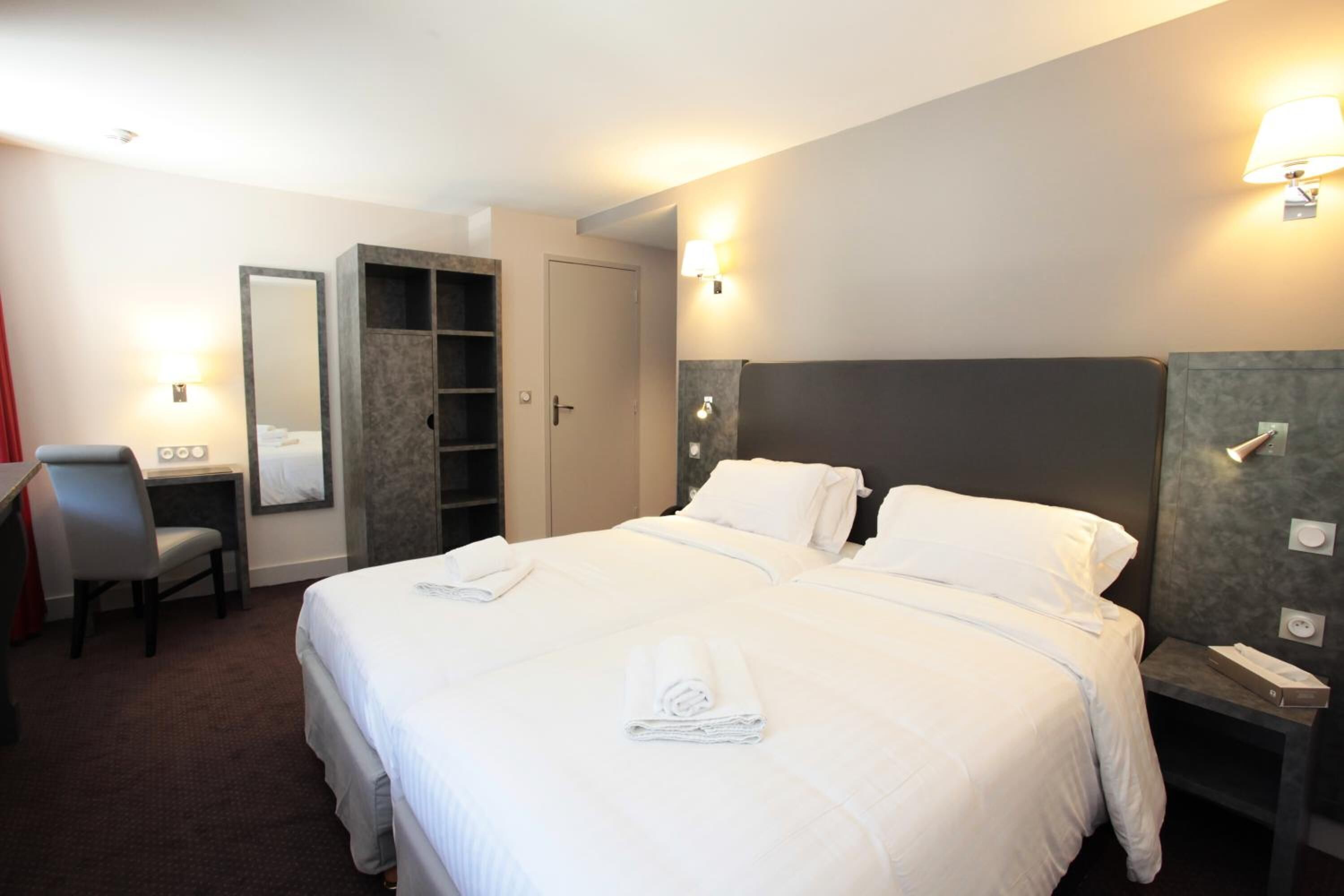 Habitación de hotel con una cama grande, un escritorio con silla, un armario y una mesita de noche con lámpara.