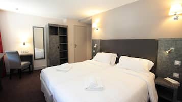 Habitación de hotel con una cama grande, un escritorio con silla, un armario y una mesita de noche con lámpara.