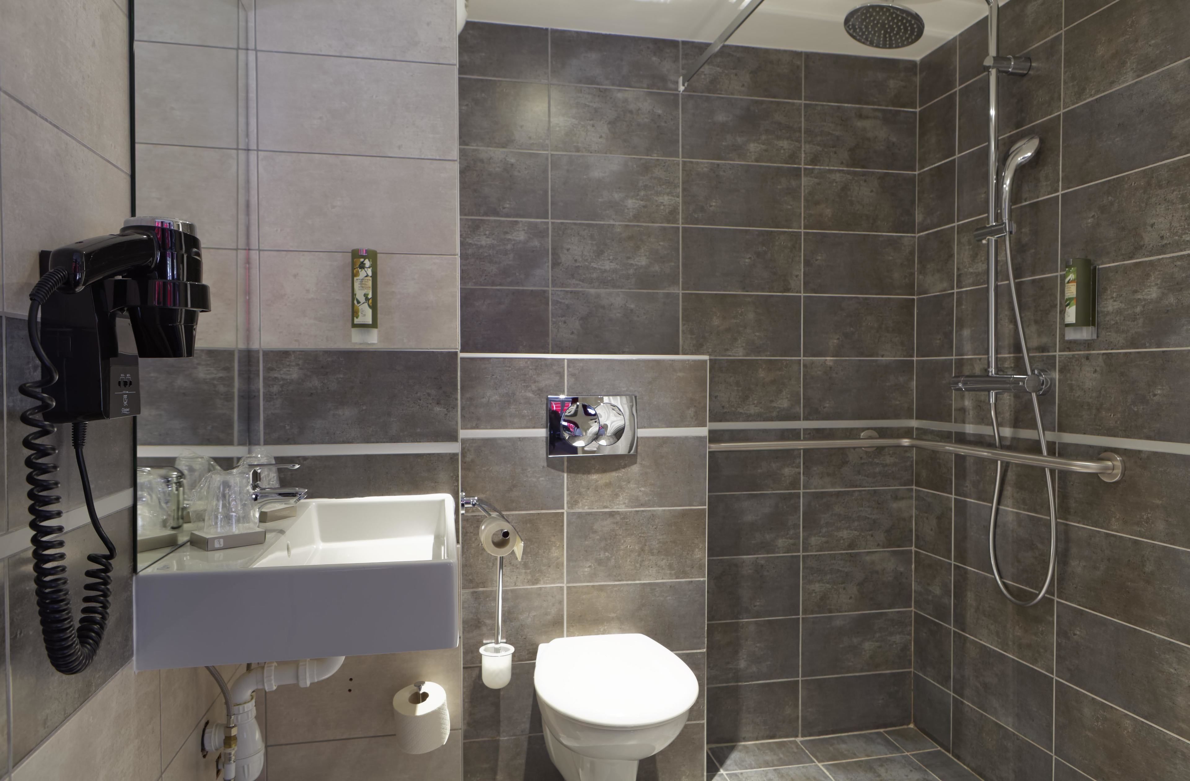 A modern bathroom with a shower, toilet, sink, and a hairdryer on the wall.