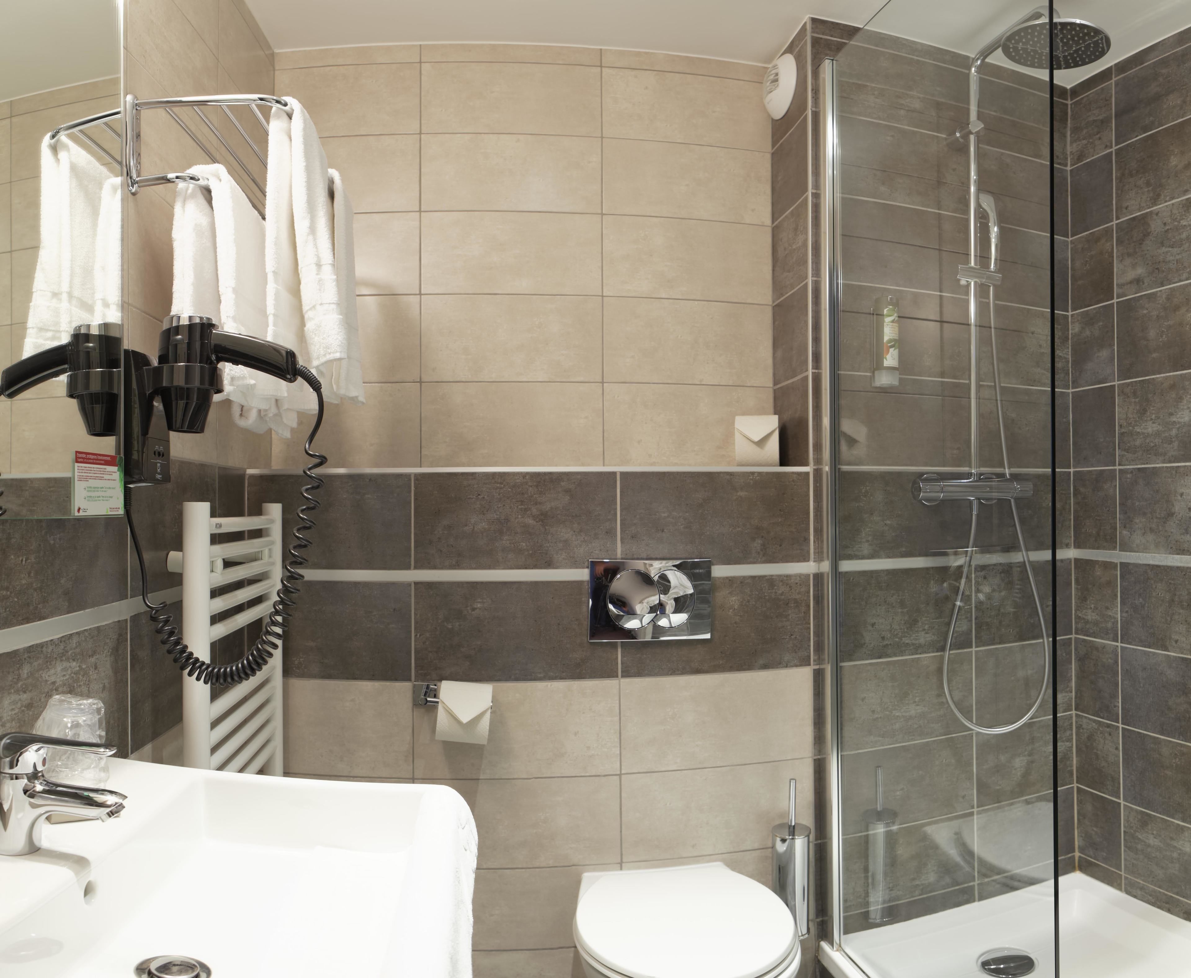 A modern bathroom with a glass-enclosed shower, a white sink, and a towel rack with several towels.